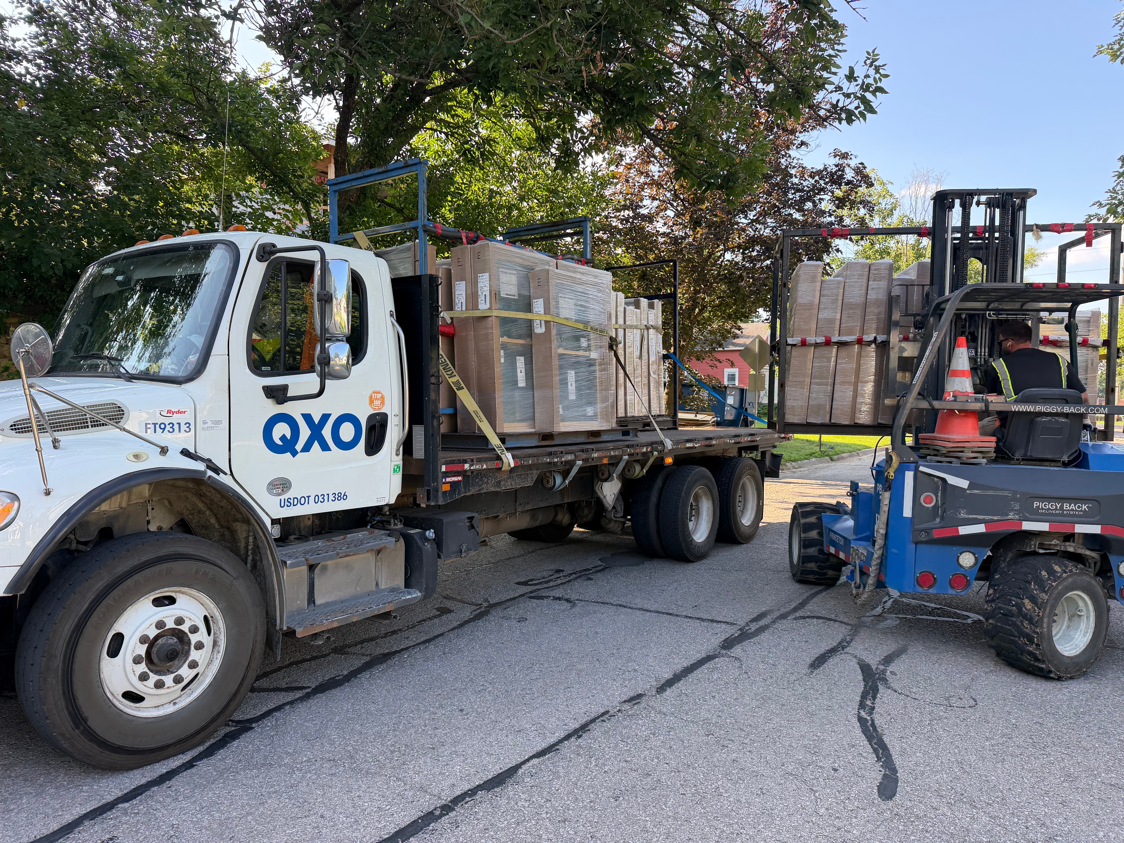 QXO delivery truck and Piggy Back forklift unloading pallets of windows and doors on site