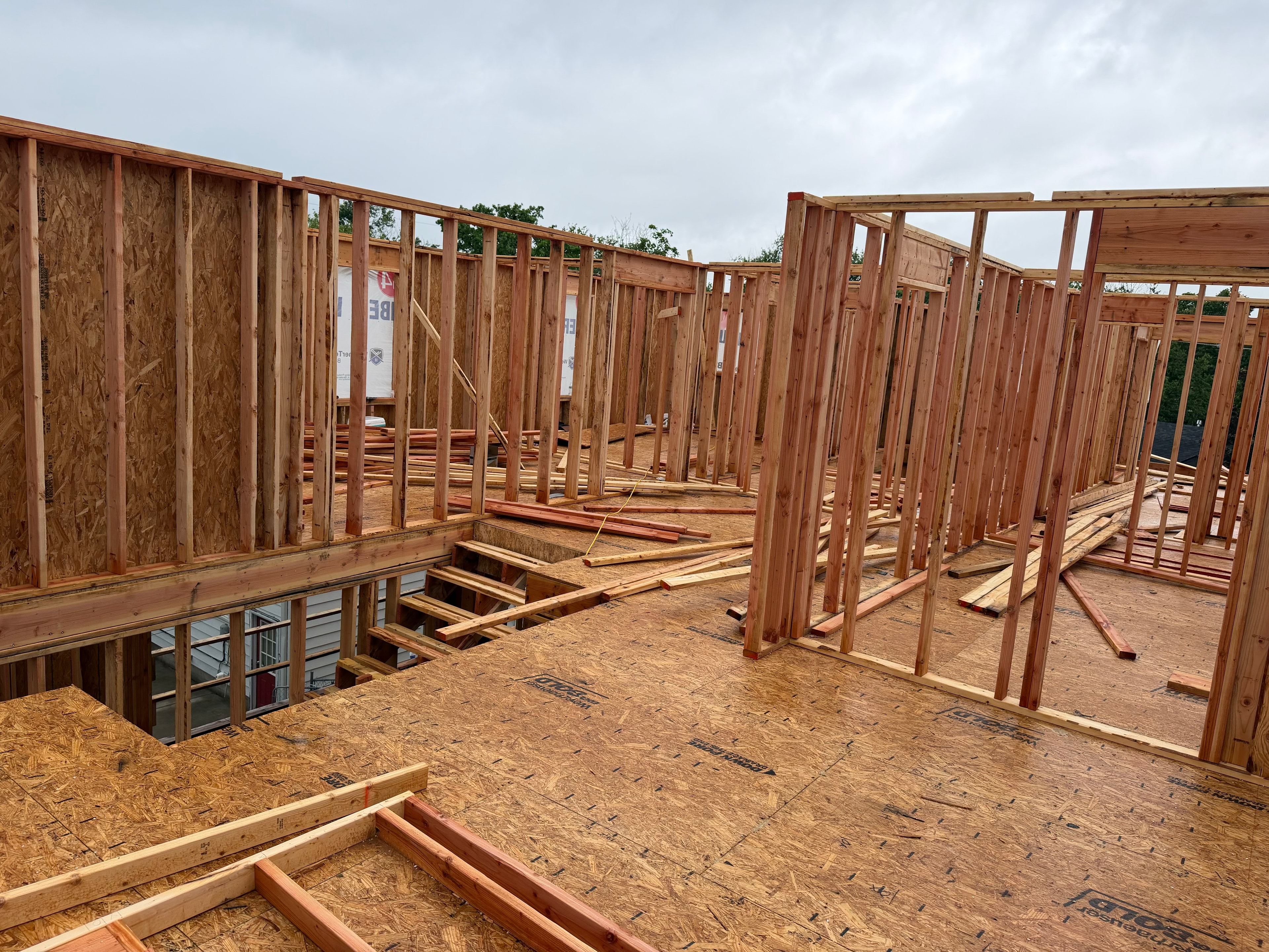 Standing on the third floor OSB subfloor — wall studs rising all around, stairwell opening cut in the floor, 84 Lumber wrap visible on the surrounding walls